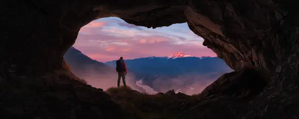 Adventurous Man Hiker standing in a cave. River and Mountains in background. Adventure Composite 3d Rendering. Aerial Image of landscape from BC, Canada. Sunset Cloudy Sky