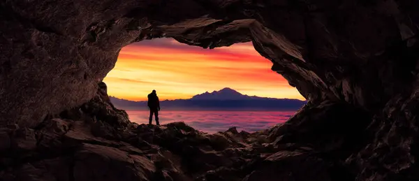 Adventurous Man Hiker standing in a cave. Fog and Mountains in background. Adventure Composite 3d Rendering. Aerial Image of landscape from BC, Canada. Sunrise Cloudy Sky