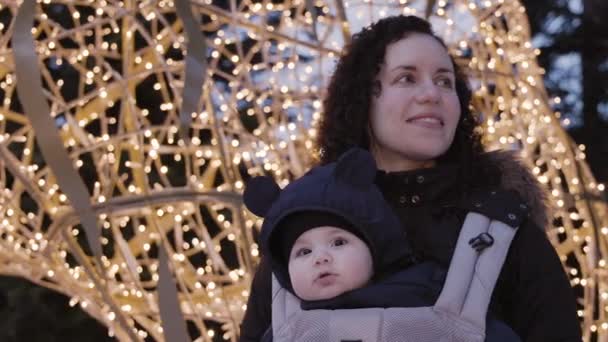 Moeder Met Schattige Baby Boy Carrier Kijkend Naar Kerstverlichting Winterseizoen — Stockvideo