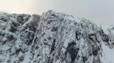 Rocky Cliffs bulutlu kış gününde karla kaplıydı. BC, Kanada. Havadan.