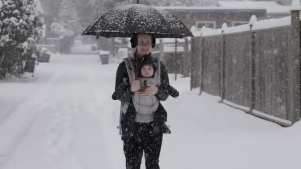 スノーウィーデーのフロントキャリアで愛らしい赤ちゃんと一緒に歩く母親 冬のシーズン 近所ウォーク バーナビー バンクーバー カナダ — ストック動画