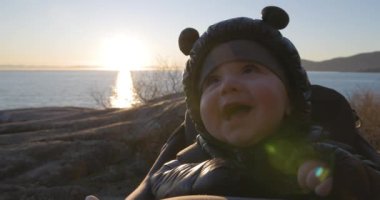 Baby Boy gülümserken, Rock 'ta okyanus manzaralı bir kargo gemisinde otururken. Gün batımı. Fener Parkı, Batı Vancouver, BC, Kanada.