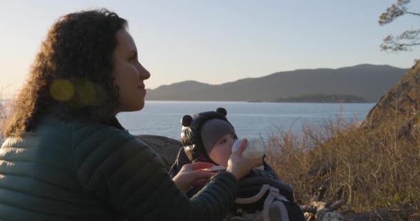 妈妈喂男婴 坐在远足的载具上 在岩石上风景秀丽的海岸边 日落了加拿大不列颠哥伦比亚省西温哥华灯塔公园 — 图库视频影像