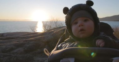 Baby Boy gülümserken, Rock 'ta okyanus manzaralı bir kargo gemisinde otururken. Gün batımı. Fener Parkı, Batı Vancouver, BC, Kanada.