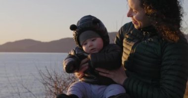 Mutlu Anne ve Oğlan 'ın gülümsediği, okyanus manzaralı bir kayanın üzerinde oturduğu yakın plan. Gün batımı. Fener Parkı, Batı Vancouver, BC, Kanada.
