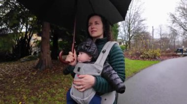 Anne ve Şirin Bebek Taşıyıcıya Karşı, Mahalle Yolunda Yürüyor. Yağmurlu bir gün, Şemsiye. Burnaby, Vancouver, BC, Kanada.