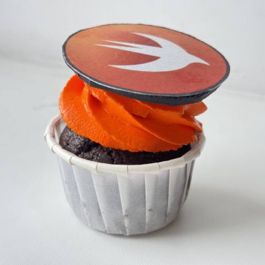 Üzerinde Swift programlama dili logosunun yer aldığı yenilebilir bir dekorasyon bulunan canlı turuncu kremalı çikolatalı kekin yakın plan görüntüsü. Programlama, teknoloji kültürü, hızlı gelişim, yazılım mühendisliği yaşam tarzı içeren temalar için ideal.