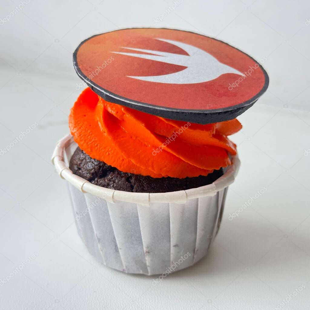 Close-up image of a chocolate cupcake with vivid orange frosting, topped with an edible decoration featuring the Swift programming language logo. Ideal for themes involving programming, tech culture, Swift development, software engineering lifestyle.