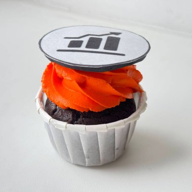 Turuncu şekerli çikolatalı kek. Üstünde de yenilebilir hisse senedi büyütme ikonu var. Beyaz arka planda, yatırımı, iş başarısını ve finansal büyümeyi eğlenceli ve yaratıcı bir şekilde sembolize ediyor..