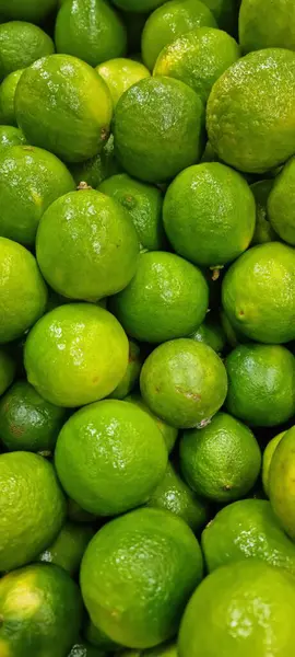Taze, parlak yeşil limon koleksiyonu. Dokulu derileri ışığı yansıtıyor. Görüntü tazelik ve doğallık hissi uyandırıyor, sağlık ve mutfak temaları için mükemmel..