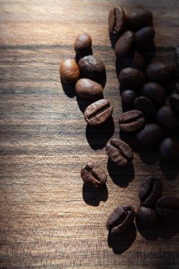 Koyu ahşap arka planda kavrulmuş kahve çekirdekleri. Kahve çekirdekleri, üzerine güneş ışığı düşen ahşap bir zemine saçılmış.