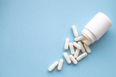 Beyaz haplar mavi arka planda beyaz şişede.