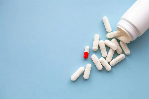 Beyaz haplar ve beyaz-turuncu bir hap mavi arka planda paketten döküldü..