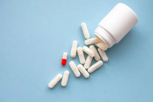 Beyaz haplar ve beyaz-turuncu bir hap mavi arka planda paketten döküldü..