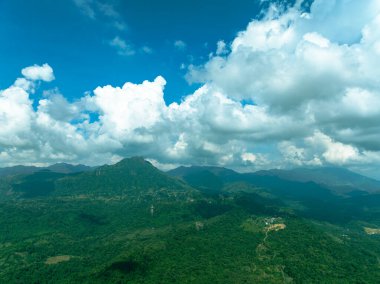 Parçalı bulutlu gökyüzünün altında yemyeşil ormanlarla kaplı tropikal bir dağ..