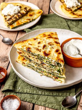 Gözleme adı verilen ıspanak ve peynirle doldurulmuş dilimlenmiş ve istiflenmiş geleneksel Türk ekmeği, bir toprak tabaktaki ekşi kremayla yuvarlak bir tabakta servis ediliyor.