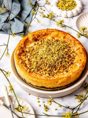 Haşhaş tohumu katmanlı Alman fırınlanmış cheesecake mermer bir masada servis edilen şam fıstığı serpiştirilmiş ve etrafına yaylı sarı dallar serpiştirilmiş.