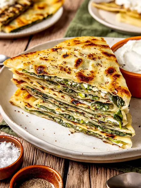 Gözleme adı verilen ıspanak ve peynirle doldurulmuş dilimlenmiş ve istiflenmiş geleneksel Türk ekmeği, bir toprak tabaktaki ekşi kremayla yuvarlak bir tabakta servis ediliyor.