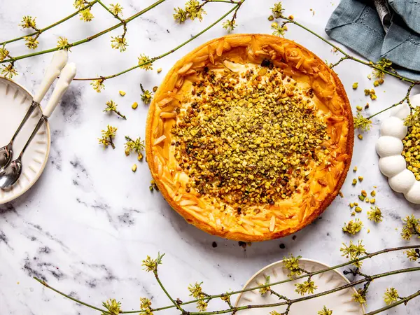 Haşhaş tohumu katmanlı Alman fırınlanmış cheesecake, bilye bir masaya fıstık serpiştirilmiş, etrafına yayılmış bahar sarısı dallar, üst manzara