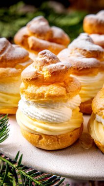 Vanilya kremalı kremalı kremalı choux pufları kapatıyoruz ve krem şanti tabakası pasta tezgahında servis ediliyor ve pudra şekeri ile toz alınıyor.