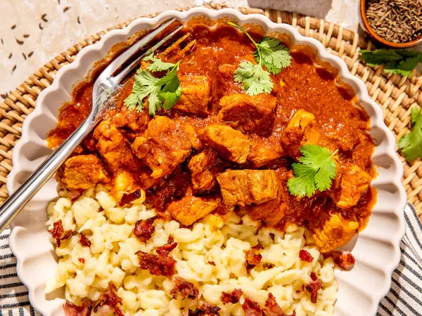 Gümüş çatallı ve üzerine taze otlar serpiştirilmiş bir kişiye servis edilen domuz eti ve ev yapımı yumurta köfteleriyle geleneksel Macar prklt güveci.