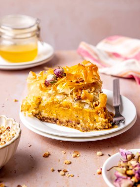 Fıstıklı dilimlenmiş Baklava peynirli kek, tatlım, ve pembe masada gümüş kaşıkla beyaz bir kek tabağında gül yaprakları.