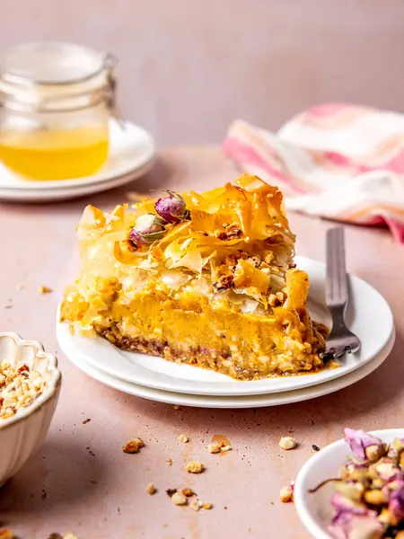 Fıstıklı dilimlenmiş Baklava peynirli kek, tatlım, ve pembe masada gümüş kaşıkla beyaz bir kek tabağında gül yaprakları.
