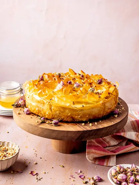 Şam fıstıklı, ballı ve gül yapraklı baklava cheesecake pembe masada servis edilir.