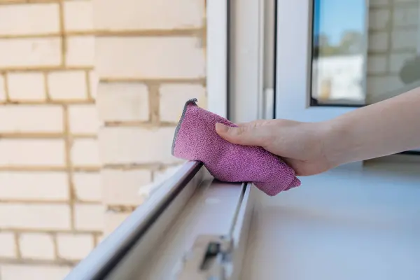 Beyaz plastik bir pencereyi elle temizleyen kişi pembe bir mikrofiber bezle, bahar temizliğini ya da ev bakımını gösteren.