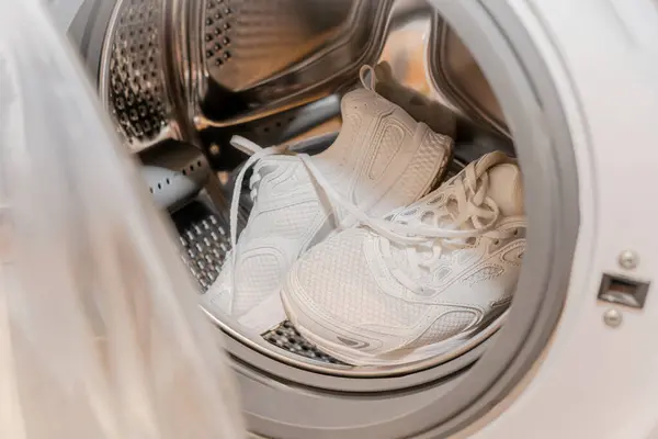 Çamaşır makinesinin içinde beyaz spor ayakkabılar. Çamaşır makinesine yerleştirilmiş temiz beyaz spor ayakkabıları, evde ayakkabı yıkama ya da çamaşır yıkama işlemini gösteriyor..