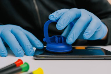 Koruyucu eldivenli bir teknisyen cep telefonunun arka kapağını sökmek, onarmak veya bakım için vakum kabı temizleme aracı kullanır..