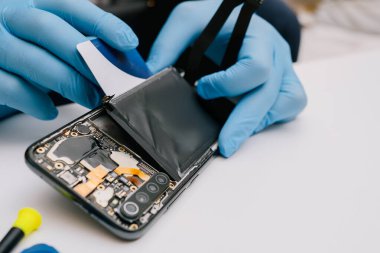 Beyaz arka planda parçalanmış bir akıllı telefon. Kayıp bir batarya karşılaştırması ve hasarlı, şişmiş bir eski. Elektronik tamir ve bakım konsepti