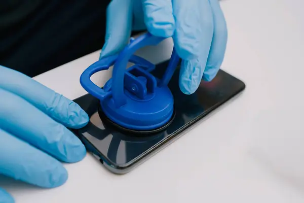 Koruyucu eldivenli bir teknisyen cep telefonunun arka kapağını sökmek, onarmak veya bakım için vakum kabı temizleme aracı kullanır..