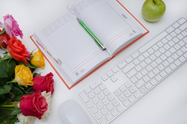 Üst manzara, beyaz masa, yeşil elma, açık planlayıcı, klavye ve fare önde, yanında renkli gül buketi, çalışma alanı, planlama, üretkenlik, ofis, organizatör, minimal stil