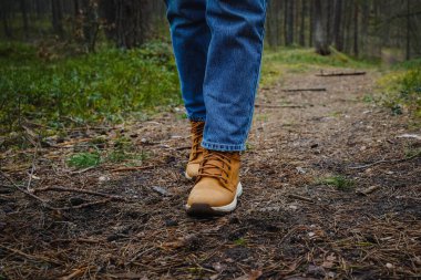 Kotlu bacakları ve yürüyüş botlarıyla ormanda yanında bir köpekle dikilen pençeleri çam iğneleriyle kaplı bir kızın yakın çekimi.
