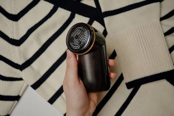 Çizgili bir kazaktan kumaş traşlı iplik çıkarmak. Süreç, yün giysileri yumuşaklık ve düzgün görünümü onarır. Sıcak bir kazağın yakın çekimi yenileniyor.