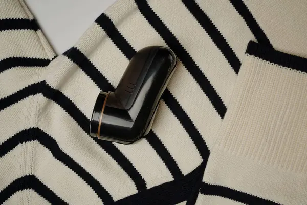 Yumuşak yün kumaşa yerleştirilmiş bir iplik çıkarıcının yakın plan görüntüsü, giysi yenileme ve bakımında kullanılan aracı vurguluyor.