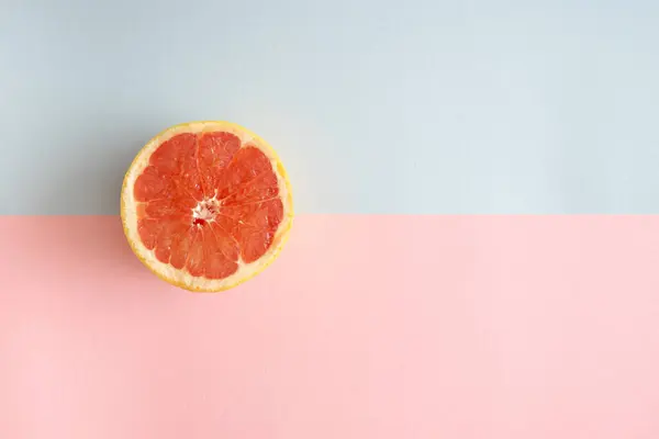 Açık pembe ve gri arka planda yarım greyfurt ve kopyalama alanı. Minimum yaz düzlüğü.