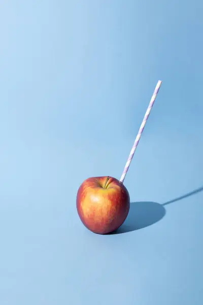 Mavi arka planda saman içen elma. Yaratıcı minimum meyve yaz konsepti.