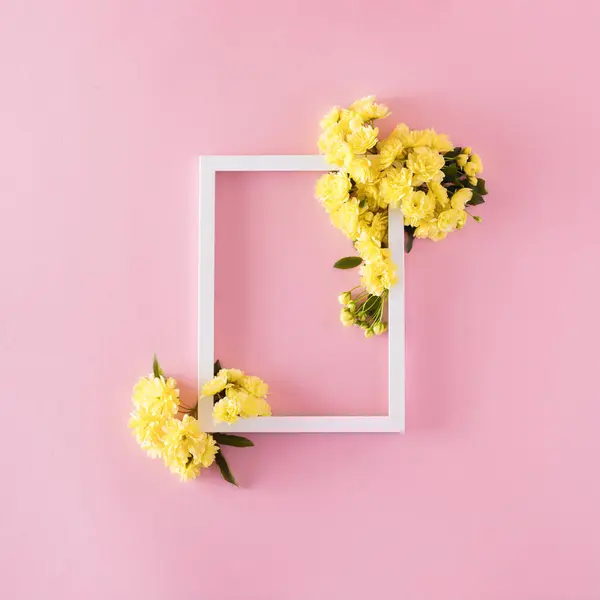 Pembe arka planda sarı çiçekli beyaz fotoğraf çerçevesi. Minimum düz konsept.