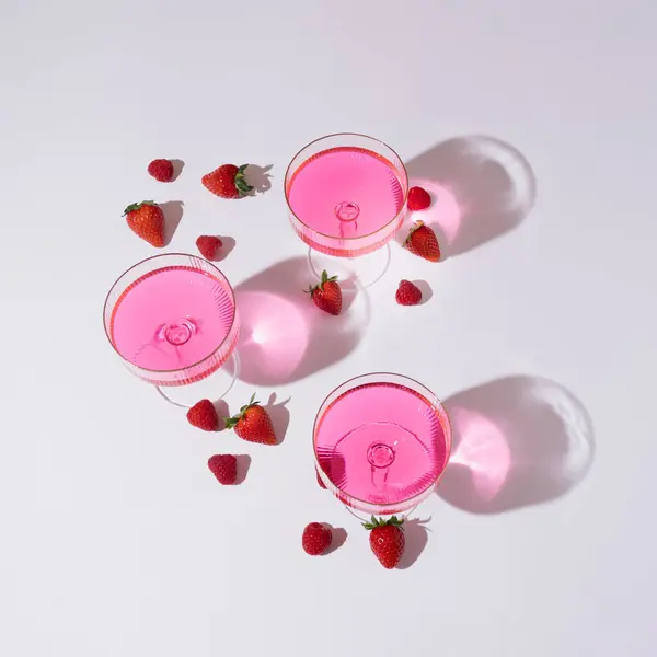 Beyaz arka planda pembe cam ve çilek eşliğinde yaratıcı bir yaz partisi konsepti.