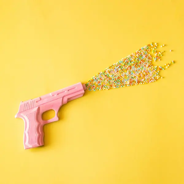 Sarı pastel arka planda pembe hippi tabancası ve renkli canlılar. Düz konsept.