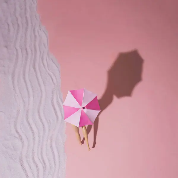Yaratıcı minimal plaj kavramı. Oyuncak bacaklı ve şemsiyeli yaz tatili düzeni pembe arka planda ve pastel mor kumlarda