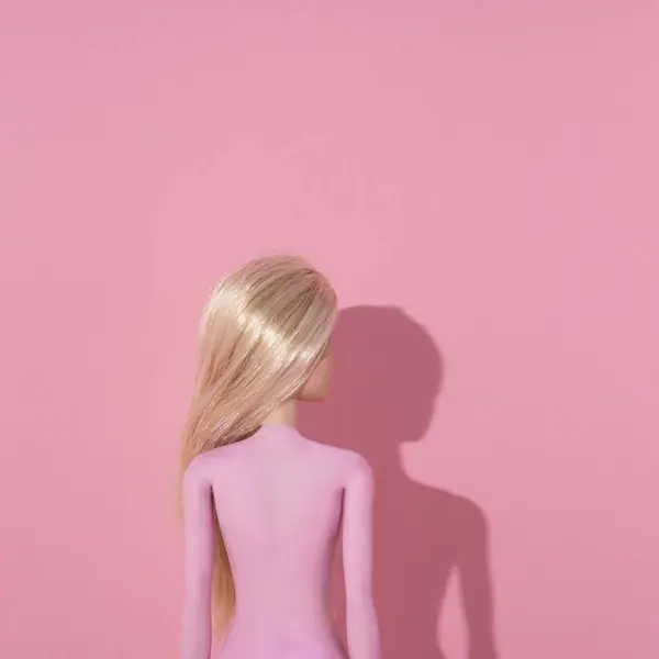 Pembe arka planda sarışın kız oyuncağı. Gölgeli yaratıcı minimum konsept.