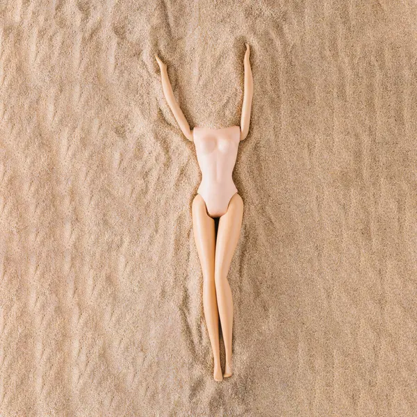 Toz renkli mayo giymiş oyuncak bebek vücudu kumda yatıyor. Yaratıcı güzellik kumsalı yaz konsepti.