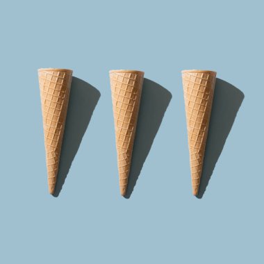 Pastel mavi arka planda üç tane güneşli dondurma külahı. Minimum yaz konsepti.