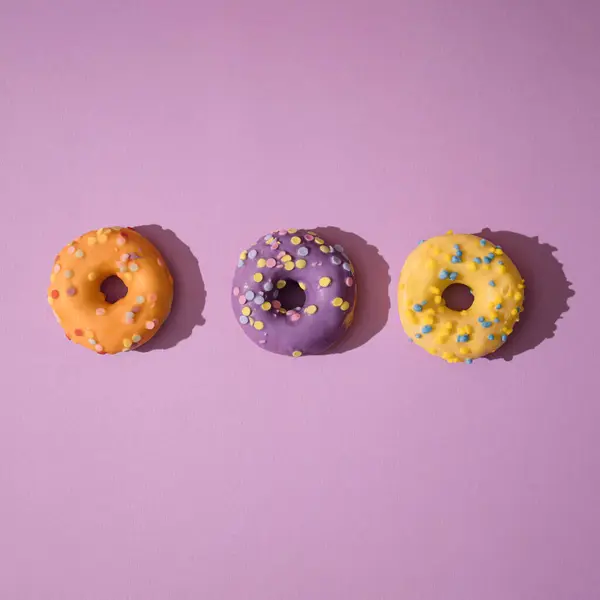 Pastel mor arka planda renkli çörekler için yaratıcı bir düzenleme. Minimum gıda kavramı.