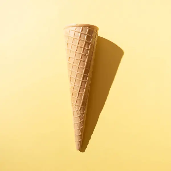 Sarı arka planda gölgesi olan güneşli dondurma külahı. Minimum yaz kavramı.