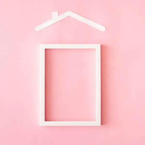 Kağıt ev çatısı ve pembe arka planda beyaz çerçeveyle yapılmış minimum emlak konsepti. Anlaşıldı.