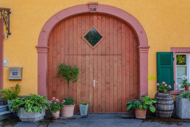 Yeşillik ve saksı bitkileriyle çevrili büyük ahşap kapılı büyüleyici bir bina, davetkar ve resimli bir giriş yaratıyor..